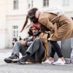 Young woman giving money to homeless beggar man sitting in city.