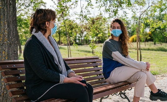 Social distance. Mother and daughter in social distancing sitting on bench in park. Pandemic. Coronavirus