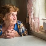 Old lonely woman sitting near the window in his house.